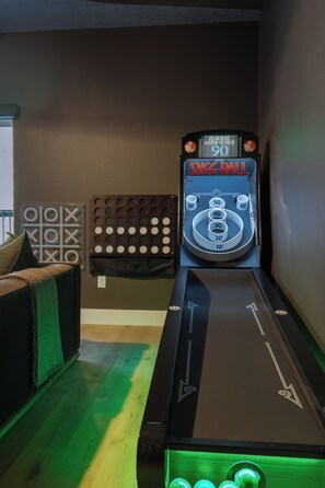 Una máquina de pinball con pantalla de puntuación digital y un dardo en una habitación con alfombra verde y un sofá.