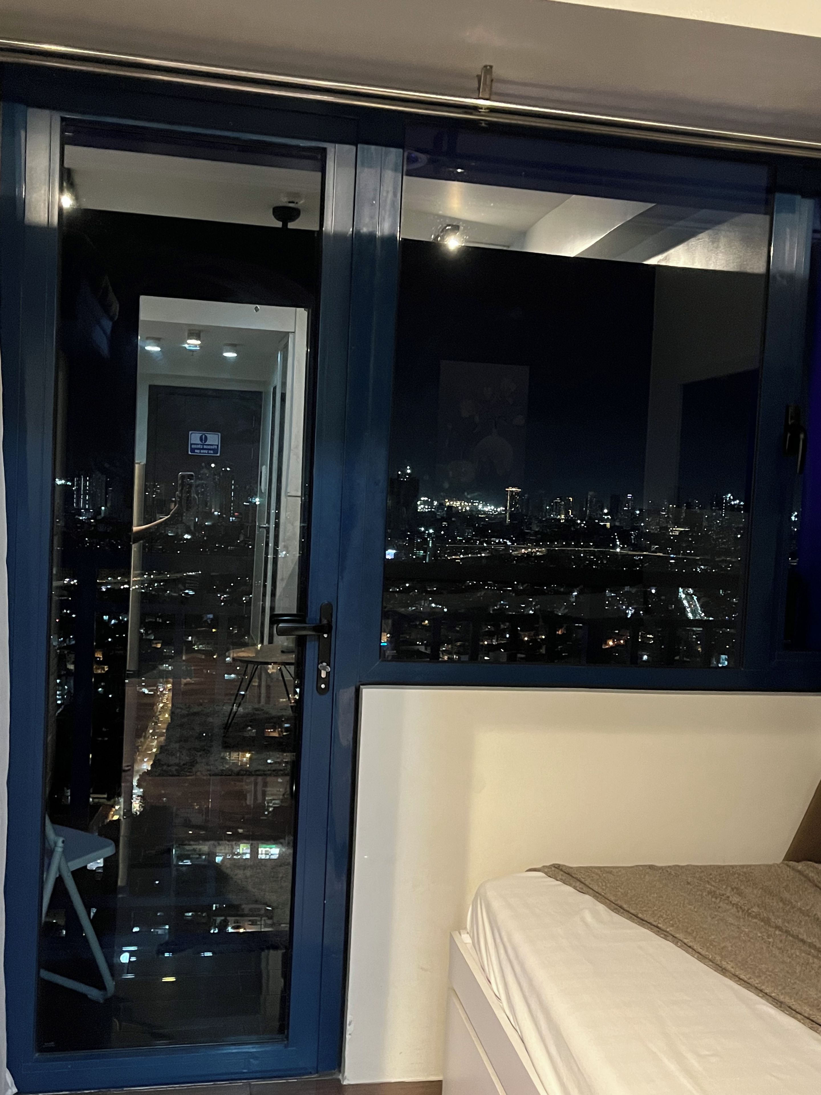 Ein Schlafzimmer mit Stadtblick durch ein großes Fenster, einem Bett und einer Tür zu einem Außenbereich.
