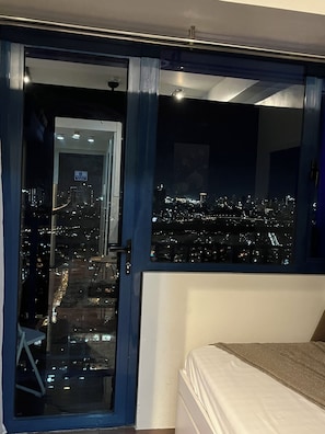 Ein Schlafzimmer mit Stadtblick durch ein großes Fenster, einem Bett und einer Tür zu einem Außenbereich.