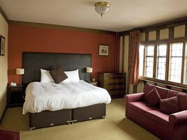 Un dormitorio con una cama grande, un aparador, un sillón rojo y una ventana con cortinas.