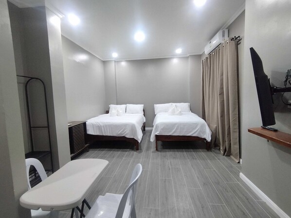 A hotel room with two beds, a desk, a chair, a TV, and a shower area.