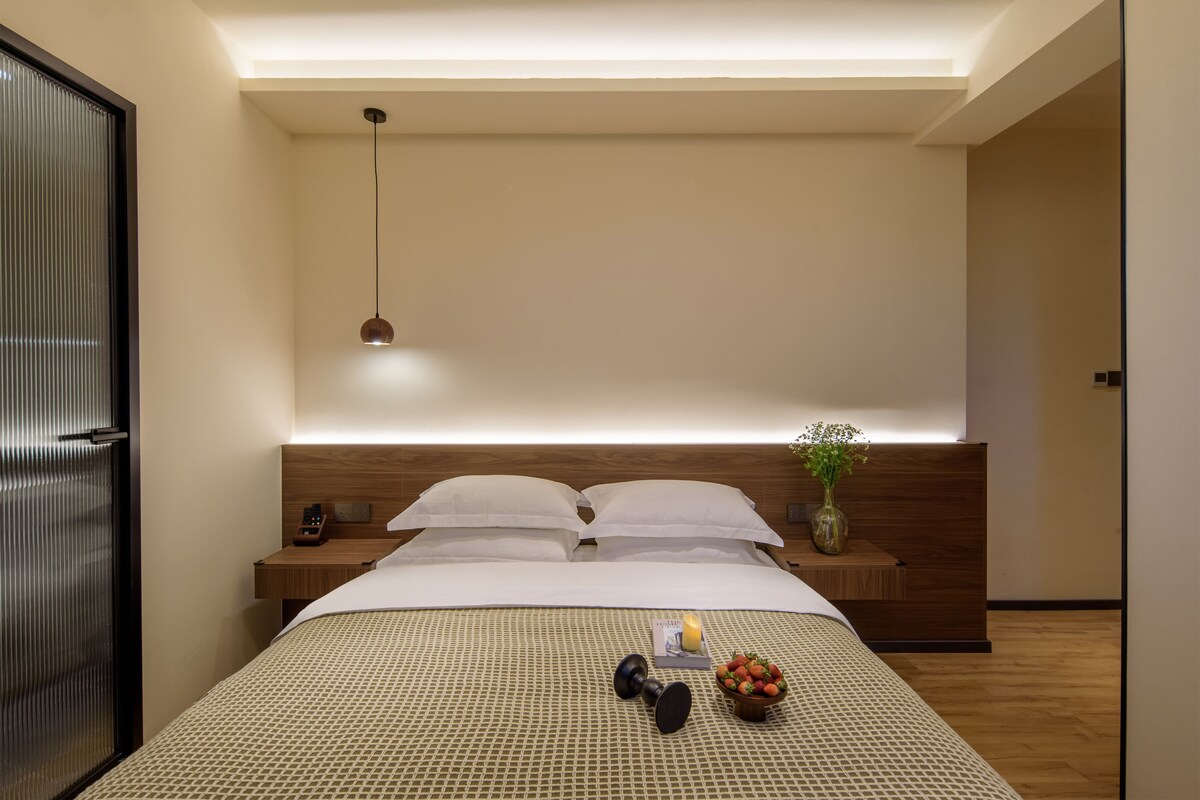 A modern hotel room with a neatly made bed, bedside tables, a bedside lamp, and a small vase with flowers.