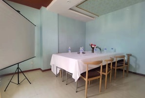 Un salón de conferencias con una mesa blanca, sillas, botellas de agua y una pantalla de proyector.