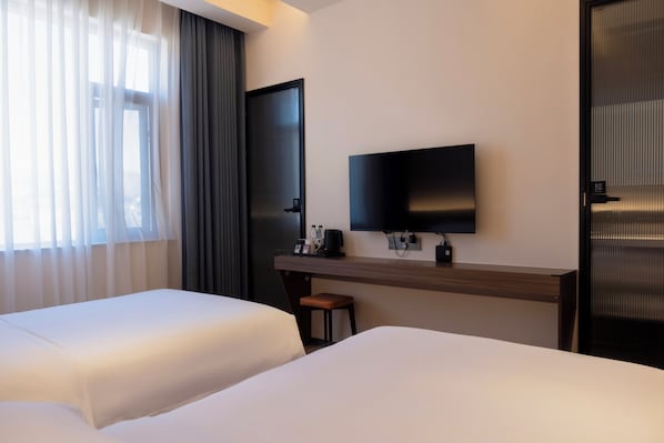 Habitación de hotel con dos camas, un escritorio, un televisor de pantalla plana, una silla y una puerta con tirador.