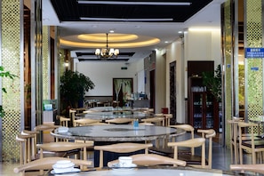 A restaurant with round tables and chairs, a chandelier, and a large painting on the wall. - Ruyi Meiju Hotel (Lijiang Dashuiche) (Lijiang)