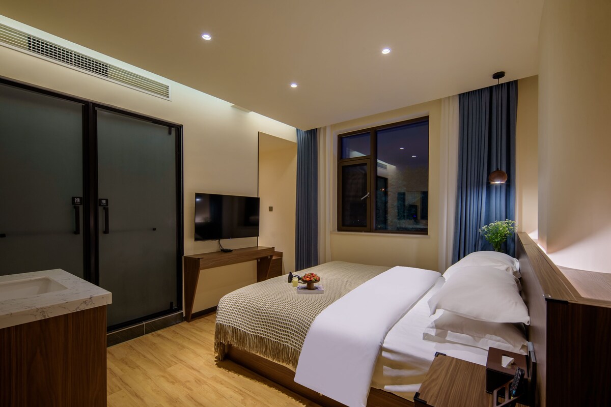 A modern hotel room with a bed, a TV, a desk, and a window with curtains.