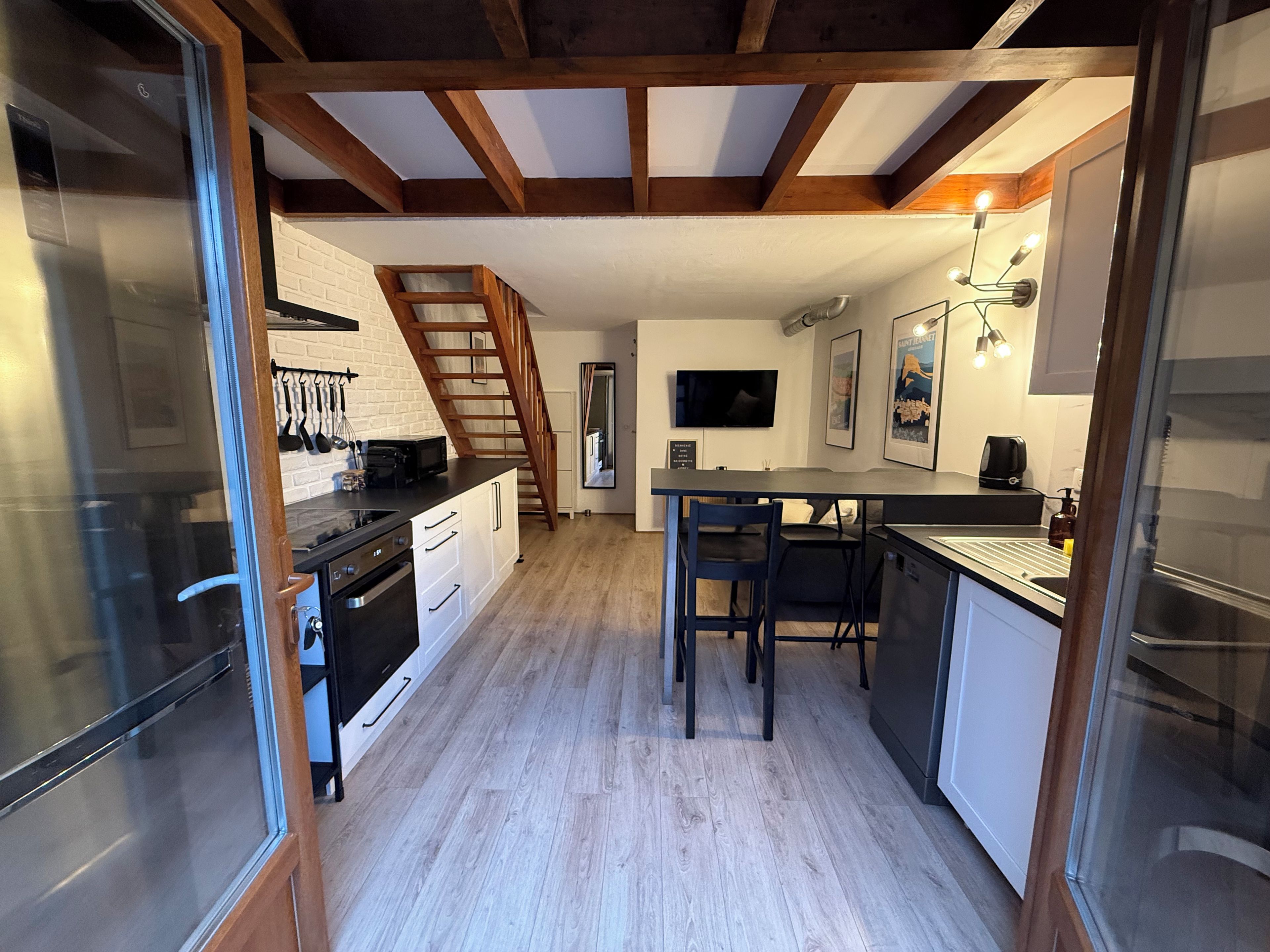 A compact kitchen with a wooden staircase, a dining area, and a TV mounted on the wall.