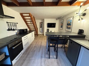 A modern kitchen with a wooden staircase, a dining area with bar stools, and a flat-screen TV mounted on the wall. - New Listing (Vence)