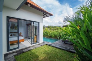 Una villa moderna con un dormitorio envuelto en vidrio, una piscina y exuberante vegetación tropical.