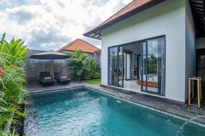 Una casa moderna con piscina, puerta de cristal y un patio con sillones de descanso.
