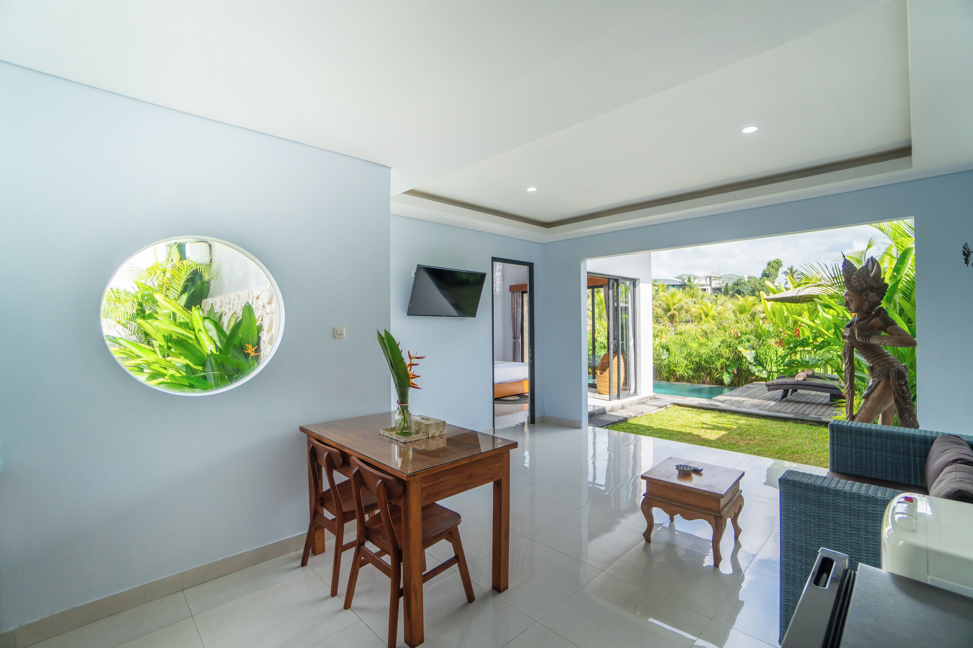 Un salon moderne comprenant un coin repas, un téléviseur fixé au mur et donnant sur un jardin luxuriant et une piscine.