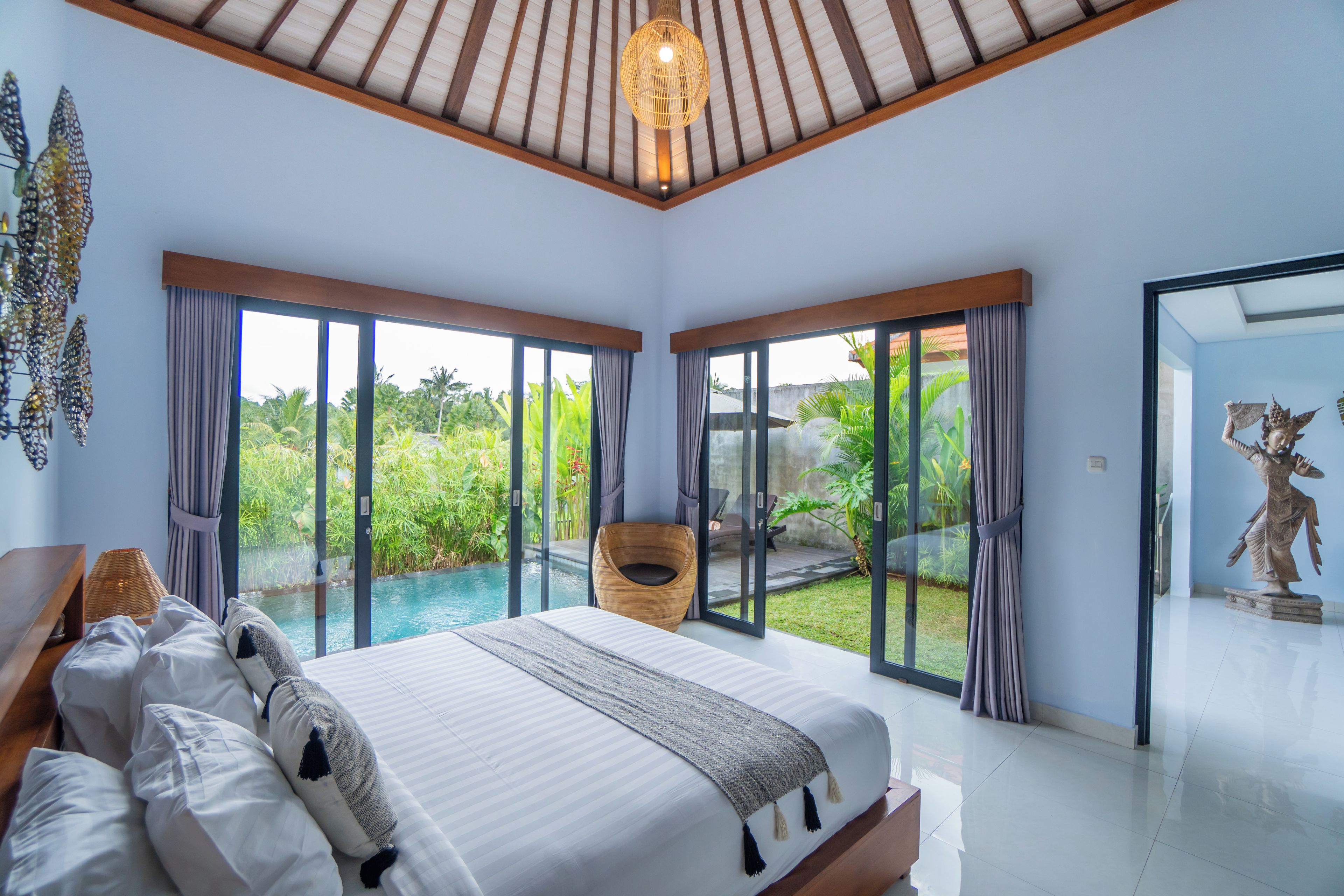 A bedroom with a large bed, a view of a swimming pool, and a statue.