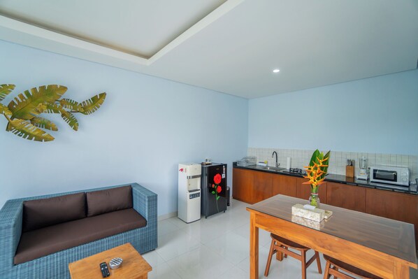 Un espacio habitable compacto con kitchenette, un sofá, una mesa de comedor y una planta decorativa.