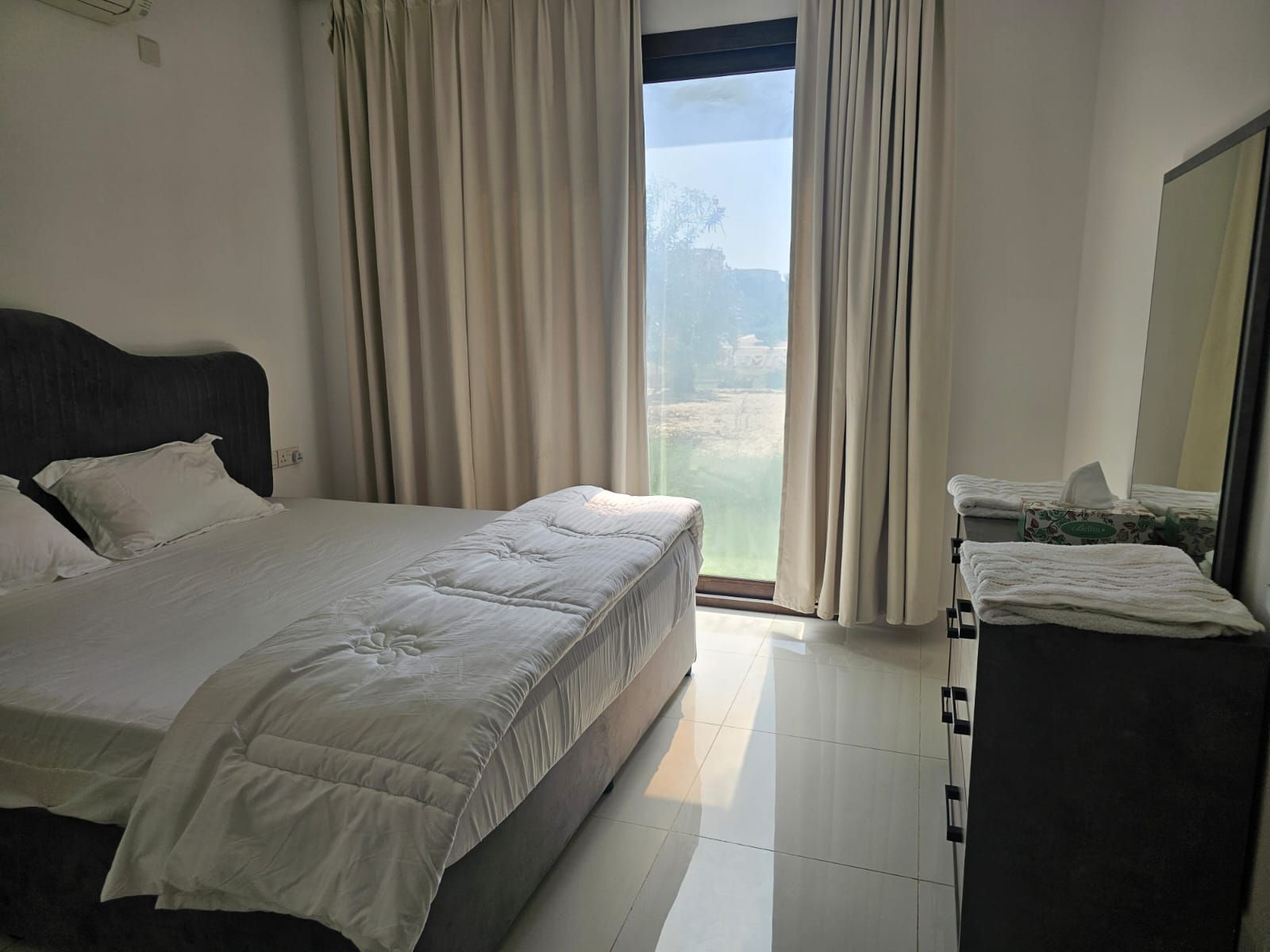 Habitación de hotel con cama, mesita de noche con caja de pañuelos y vista a un paisaje por la ventana.