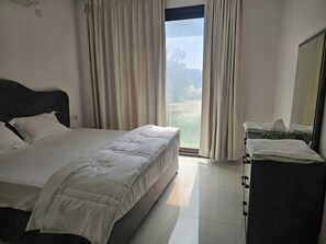 Habitación de hotel con cama, mesita de noche con caja de pañuelos y vista a un paisaje por la ventana.