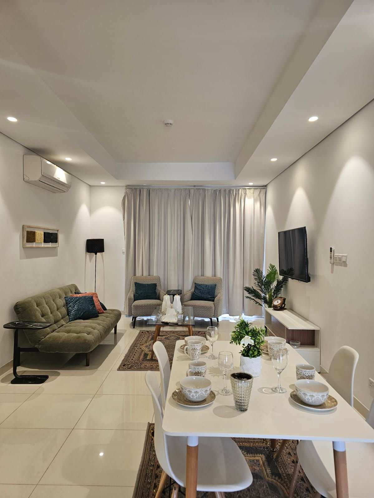 Una sala de estar moderna con comedor, que incluye un sofá, dos sillones, una mesa de centro y un televisor montado en la pared.