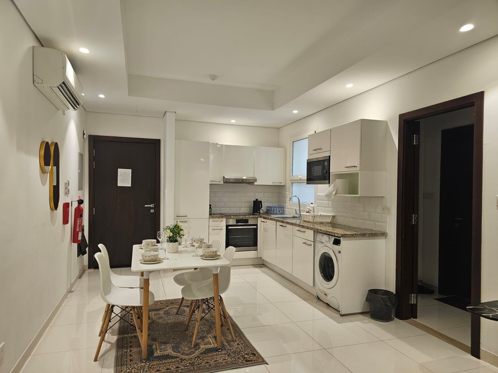 Une cuisine compacte avec des meubles blancs, un four à micro-ondes, un lave-linge et un coin repas comprenant une table et des chaises.