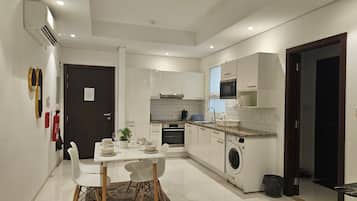 Une cuisine compacte avec des meubles blancs, un four à micro-ondes, un lave-linge et un coin repas comprenant une table et des chaises.