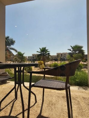 Un patio con una mesa y una silla, con vista a un área ajardinada con palmeras y edificios.