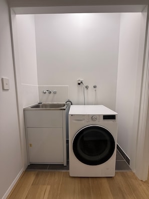 A laundry room with a washing machine and a sink. - Oasis Apartments Townsville (Garbutt)