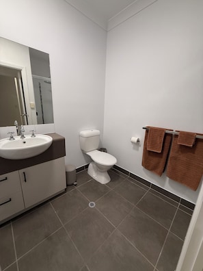 A bathroom with a white sink, toilet, and a mirror. There are towels hanging on the wall. - Oasis Apartments Townsville (Garbutt)