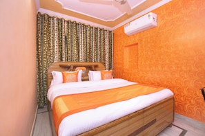 Una camera d'albergo con un letto in legno, un'ampia finestra con tende, un condizionatore d'aria e una parete decorata.