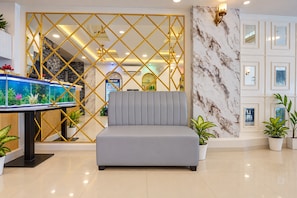 Un moderno vestíbulo de hotel con un sofá tapizado gris, un separador decorativo dorado y un gran acuario.