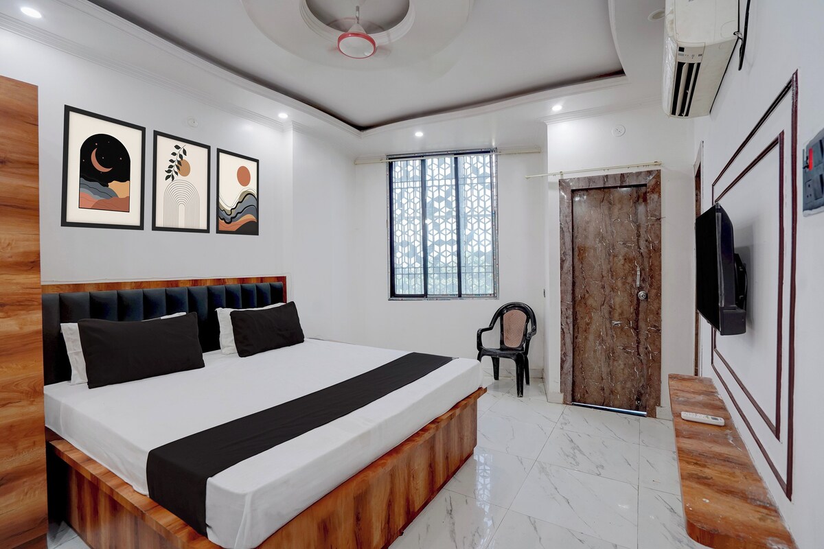 Un dormitorio moderno con una cama grande, cabecera de madera, televisor montado en la pared y una ventana con diseño geométrico.