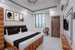 Un dormitorio moderno con una cama grande, cabecera de madera, televisor montado en la pared y una ventana con diseño geométrico.