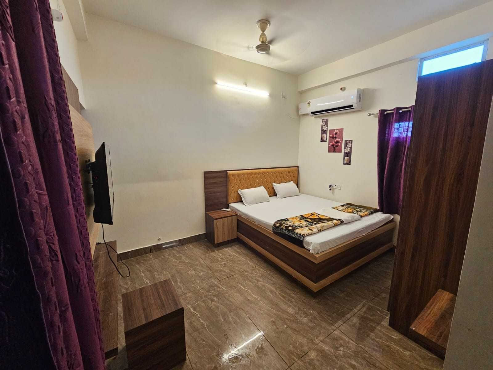 A hotel room with a bed, a nightstand, an air conditioning unit, a ceiling fan, and a TV mounted on the wall.
