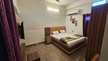 A hotel room with a bed, a nightstand, an air conditioning unit, a ceiling fan, and a TV mounted on the wall.
