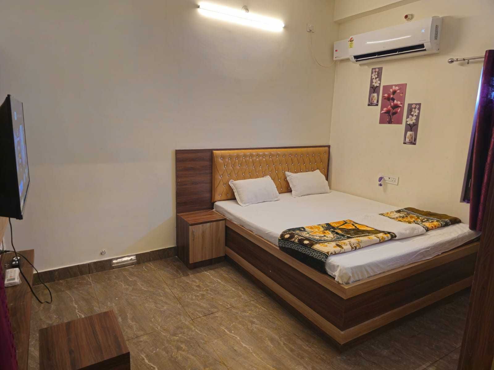 A neatly arranged hotel room with a bed, bedside tables, an air conditioning unit, and a television.