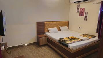 A neatly arranged hotel room with a bed, bedside tables, an air conditioning unit, and a television.