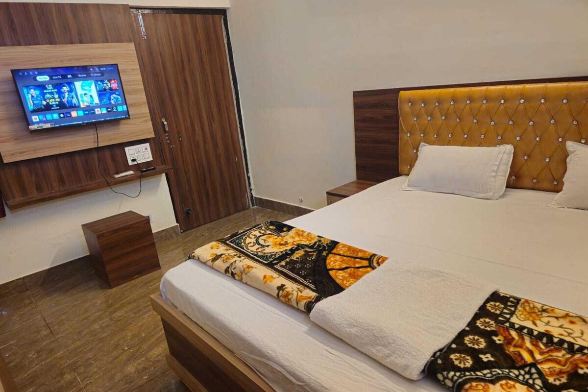 Habitación de hotel con cama, televisor montado en la pared y piso de madera.