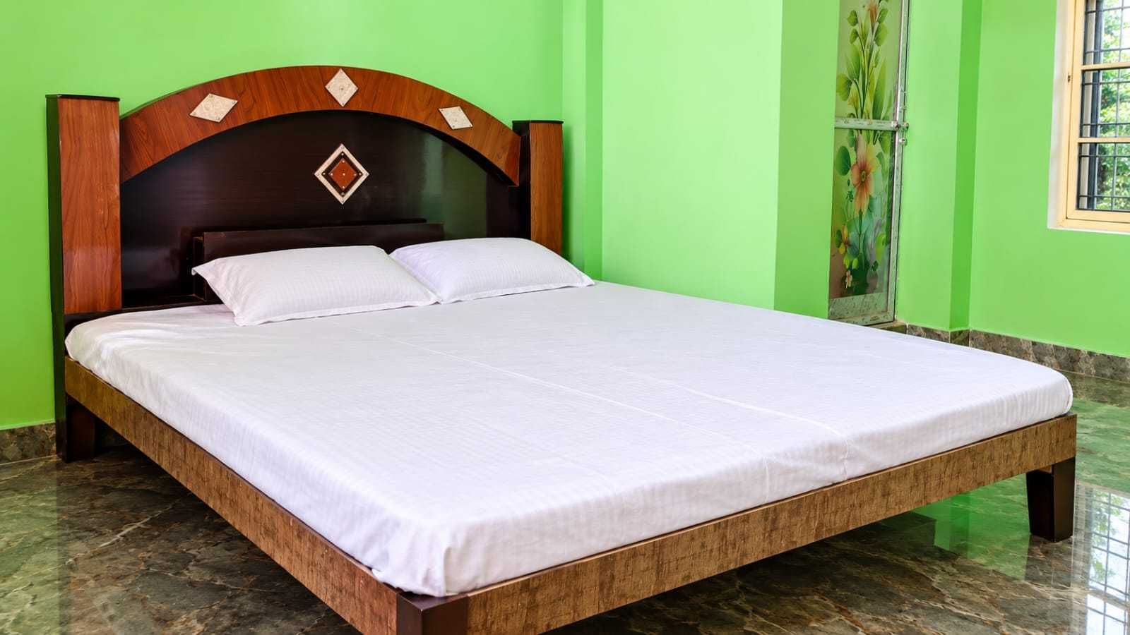 A bed with a wooden frame and a white mattress in a room with green walls and a marble floor.
