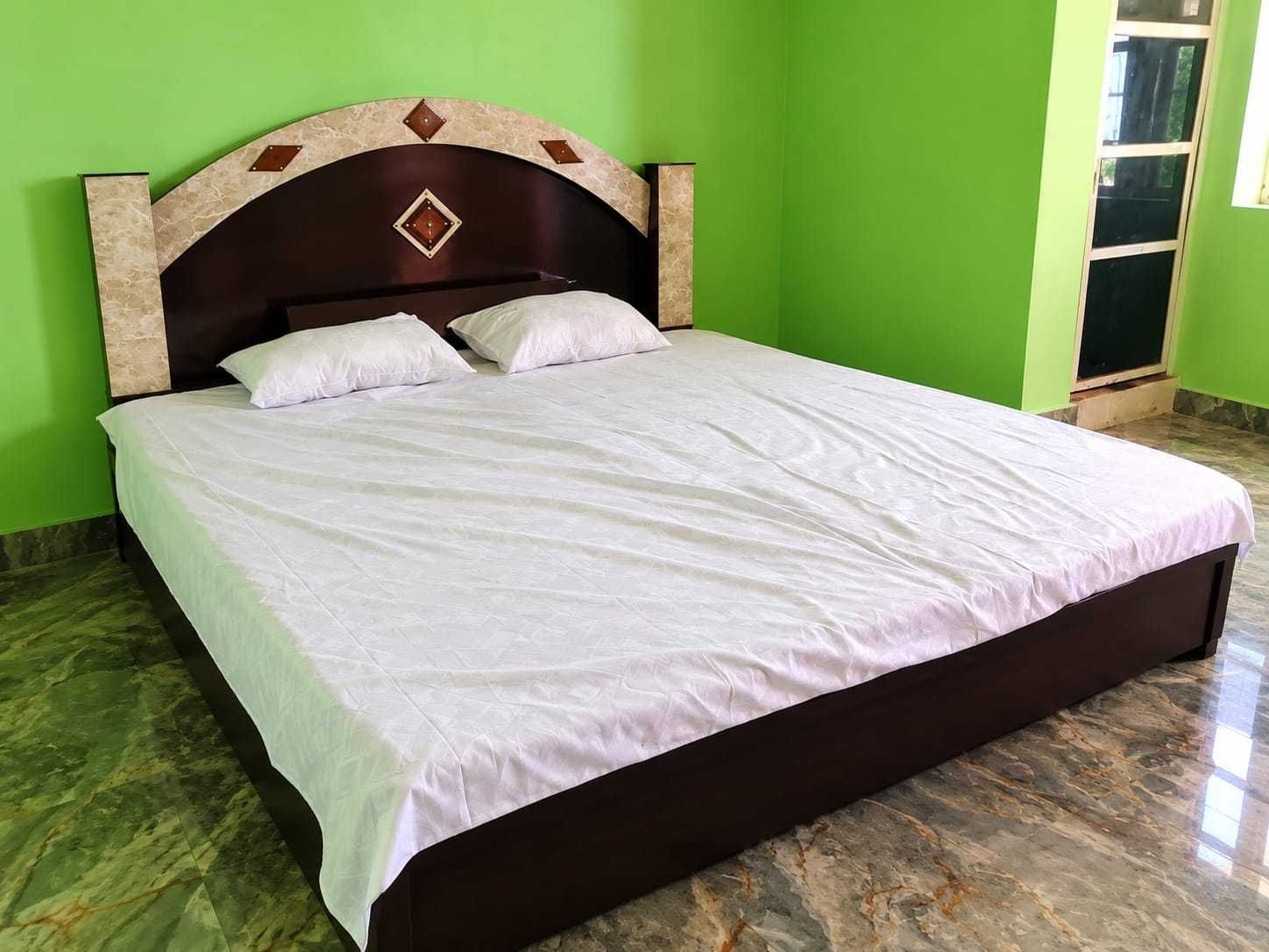 Una cama individual con cabecera oscura y ropa de cama blanca en una habitación con paredes verdes y suelo de mármol.