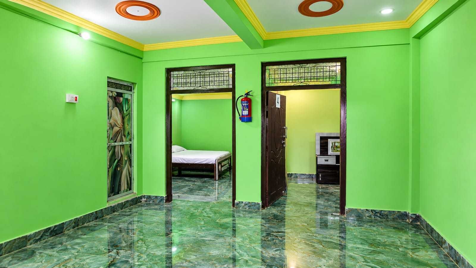 Una habitación con paredes verdes, una cama, una puerta y un mueble pequeño.