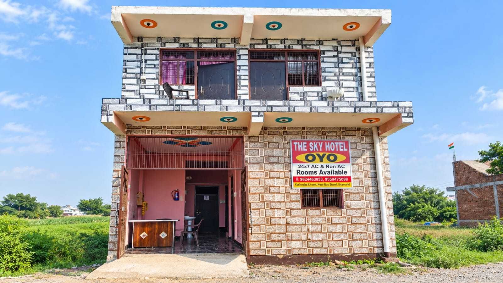 A two-story building with a sign advertising 'The Sky Hotel Oyo' offering 24x7 AC & Non AC rooms.