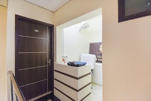 A hotel room with a dark wooden door labeled '101', a white reception desk with a blue folder, and a wall-mounted fan.