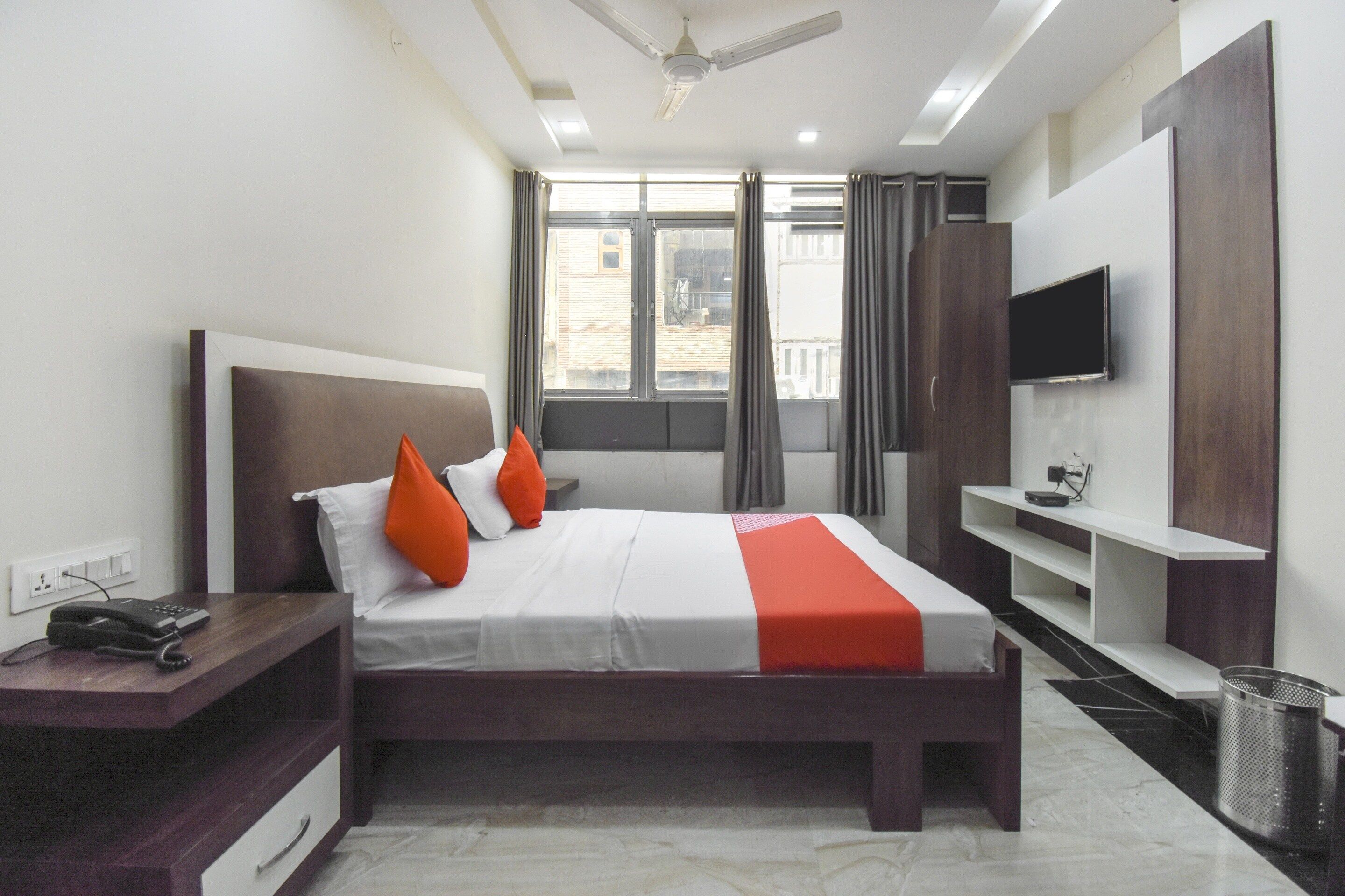A modern hotel room with a bed, a desk, a TV, and a window with curtains.