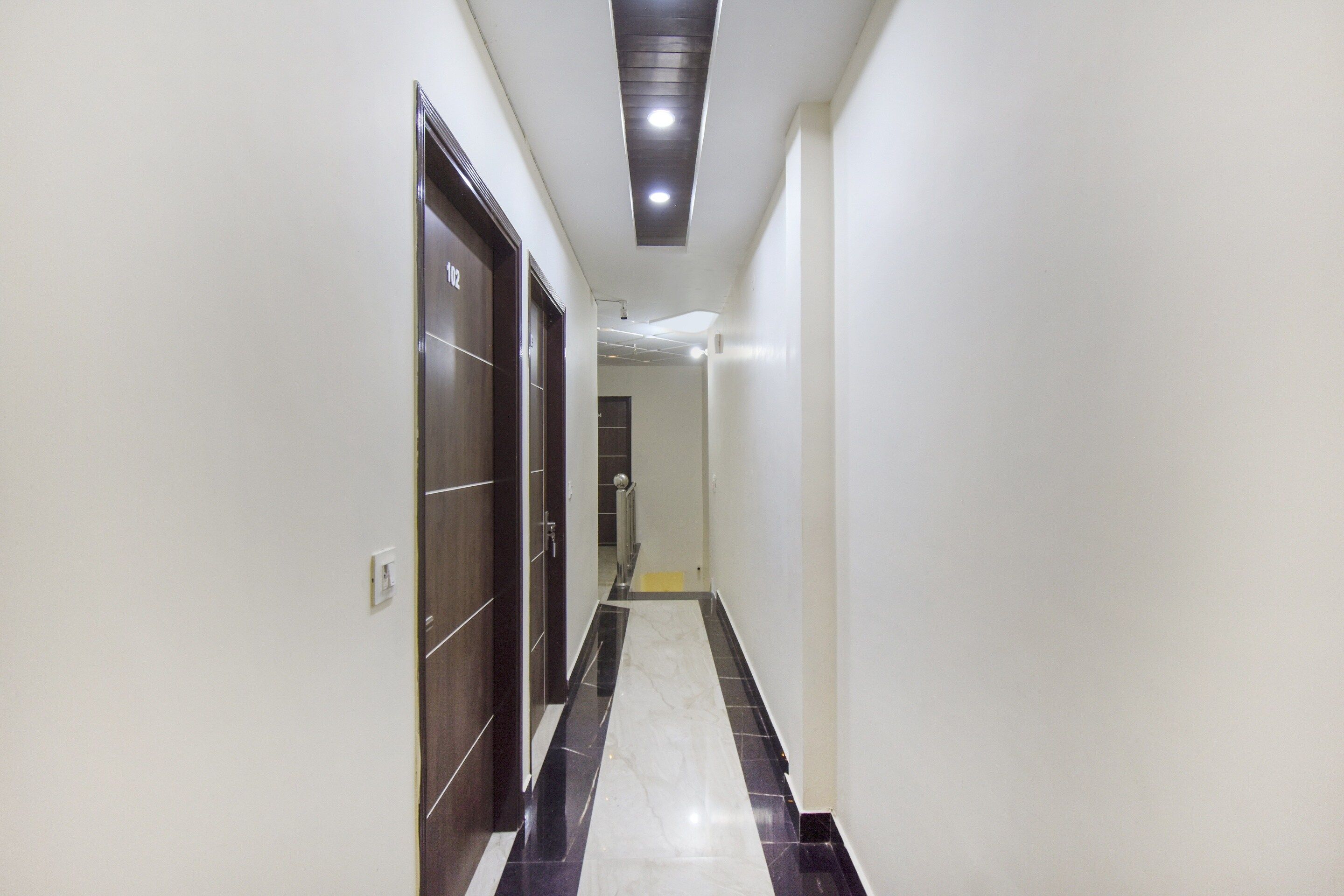 A corridor with a tiled floor, a door on the left, and a light fixture on the ceiling.