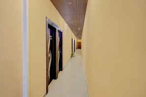 A long, narrow hotel corridor with doors on one side and a plain wall on the other. - Hotel O Eden Stay (Bilaspur)