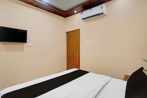 A bedroom with a bed, a wooden door, an air conditioning unit, and a television mounted on the wall. - Hotel O Eden Stay (Bilaspur)