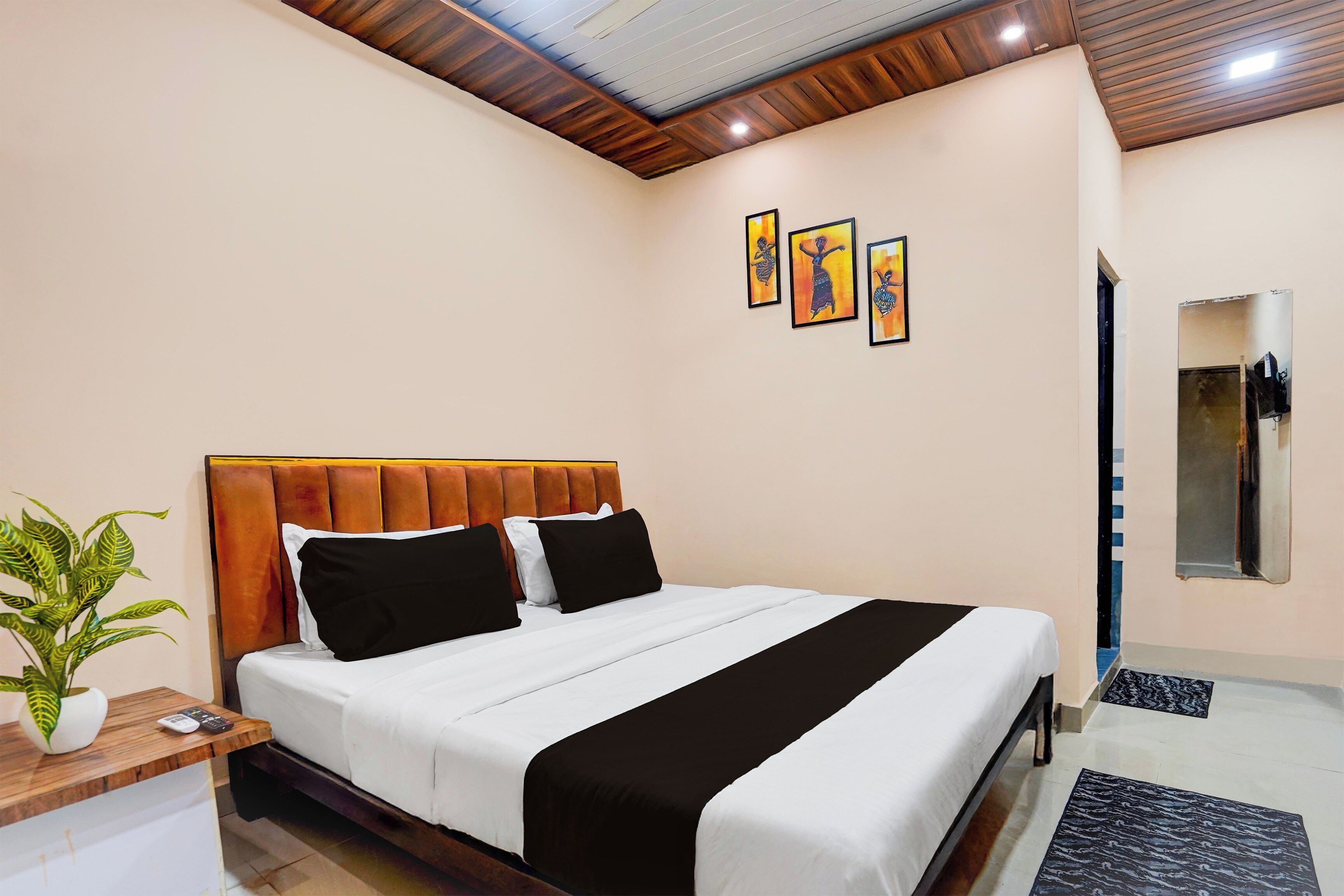 A hotel room with a bed, a bedside table with a plant, and artwork on the wall.