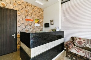 A reception area with a wooden wall pattern, a reception desk, a closed door, a flat-screen TV, and a patterned sofa. - Hotel O Apple Inn (Bharatpur)