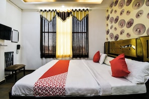 A hotel room with a bed, a chair, a TV, and a patterned wall. - Hotel O Apple Inn (Bharatpur)