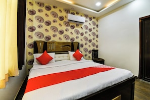 A hotel room with a bed, a nightstand, an air conditioning unit, and a patterned wall. - Hotel O Apple Inn (Bharatpur)