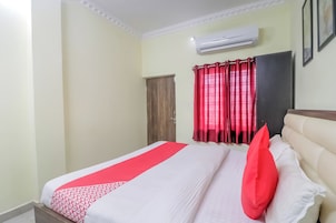 Quarto de hotel com cama, janela com cortinas vermelhas, ar condicionado e porta.