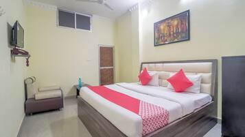 A hotel room with a bed, a bedside table, a chair, a ceiling fan, a painting on the wall, and a window.