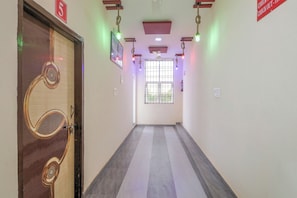 A hallway with a wooden door, a ceiling fan, and a window with metal bars. - Hotel O The Royal King (Bilaspur)